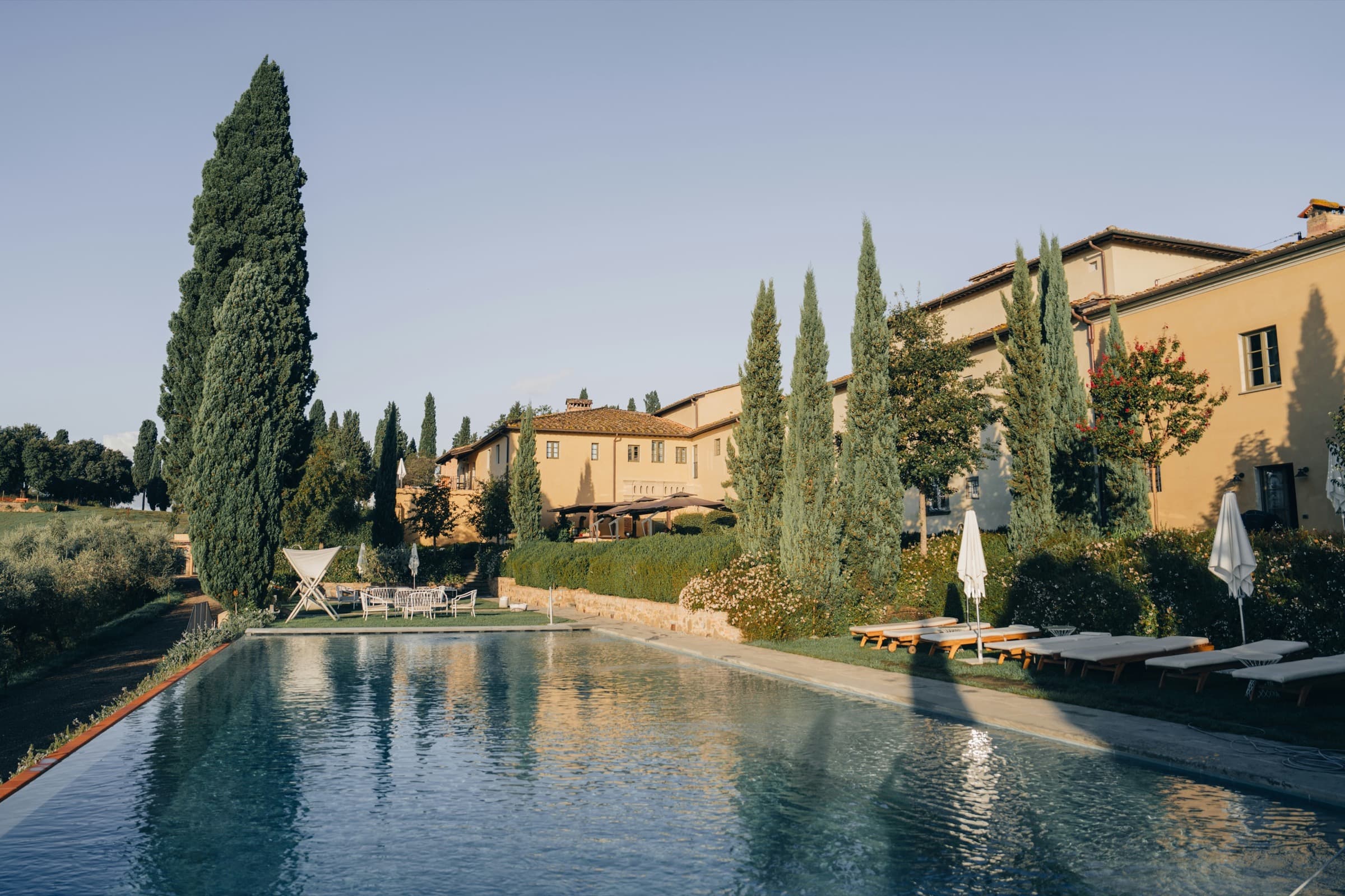 Golden-hour view of an Italian stone villa surrounded by cypress trees and gardens